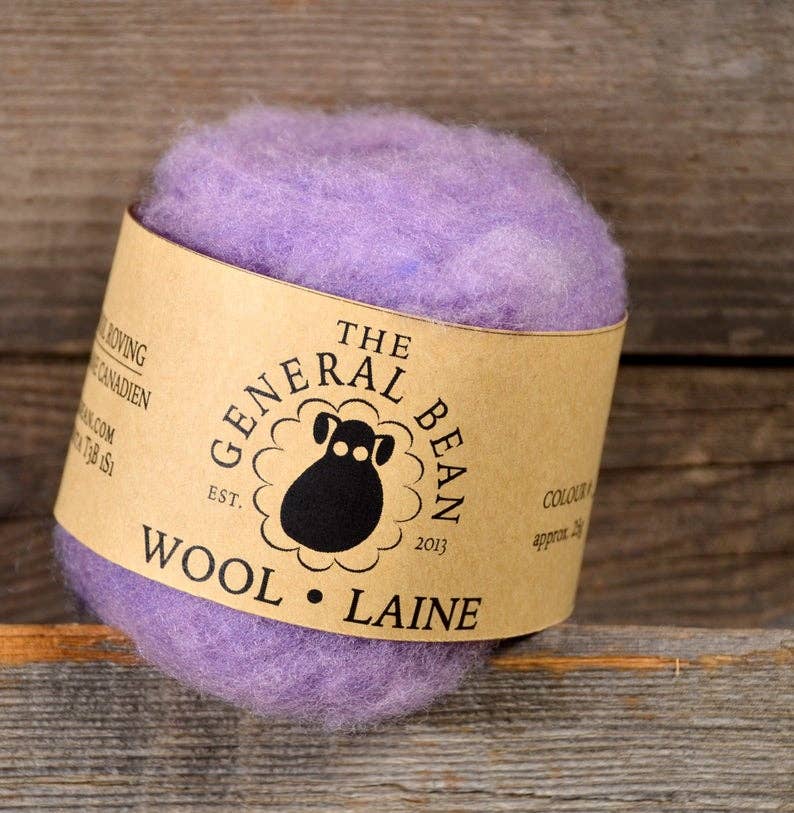 Light purple ball of wool roving with a 'The General Bean' label on a wooden background